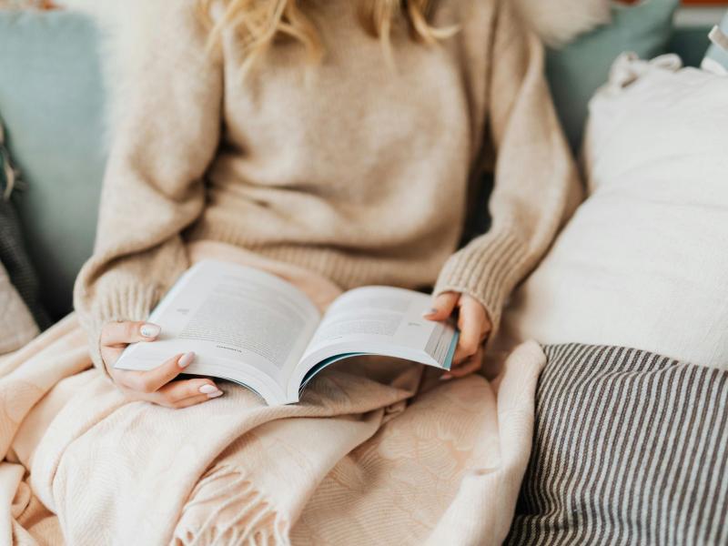 Kvinde læser i sofaen med et tæppe over sig.