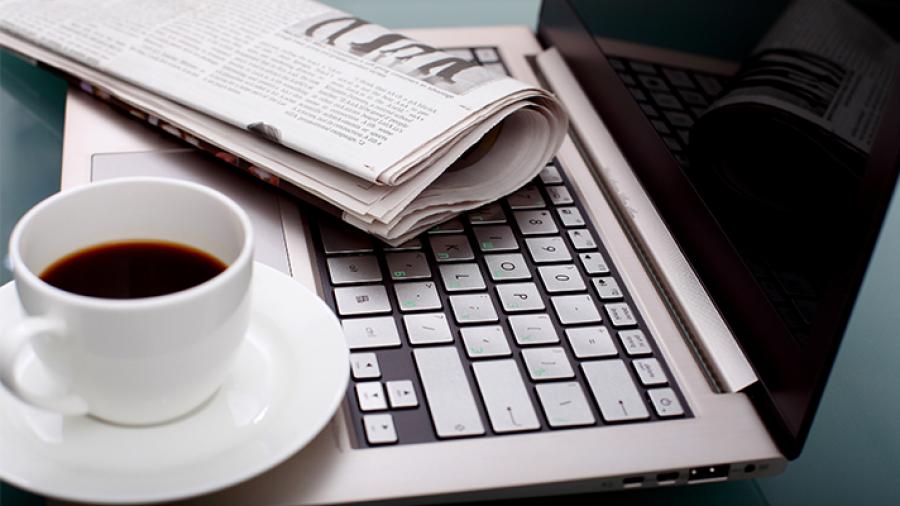 Sammenfoldet avis åben computer og en kop kaffe